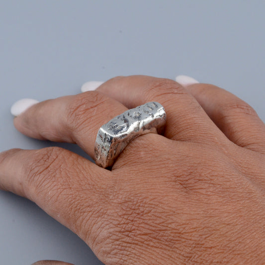 Hand wearing a square silver ring on a gray background