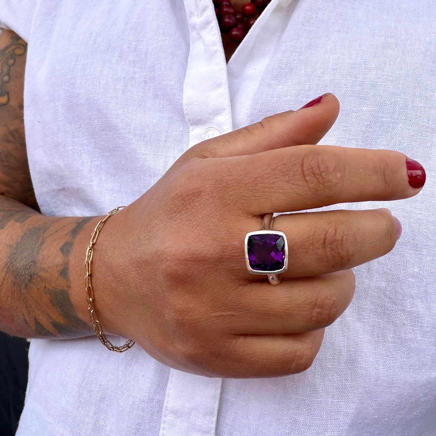 Hand wearing a purple gemstone ring with a white shirt in the background