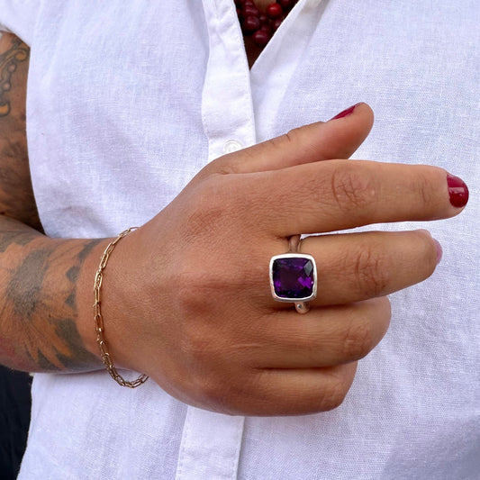 Hand wearing a purple gemstone ring with a white shirt in the background